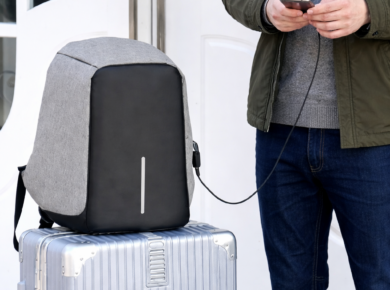 Чоловік тримає смартфон, підключений до рюкзака для ноутбука з USB-портом, який стоїть на валізі